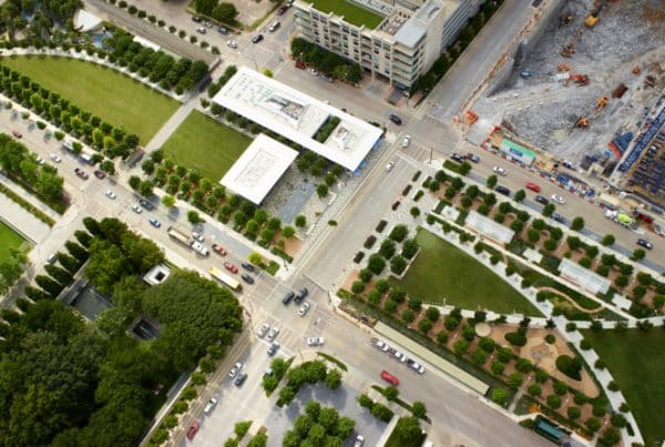 Aerial view of urban park with pathways, modern pavilion, and roads, showcasing city planning and green space integration.