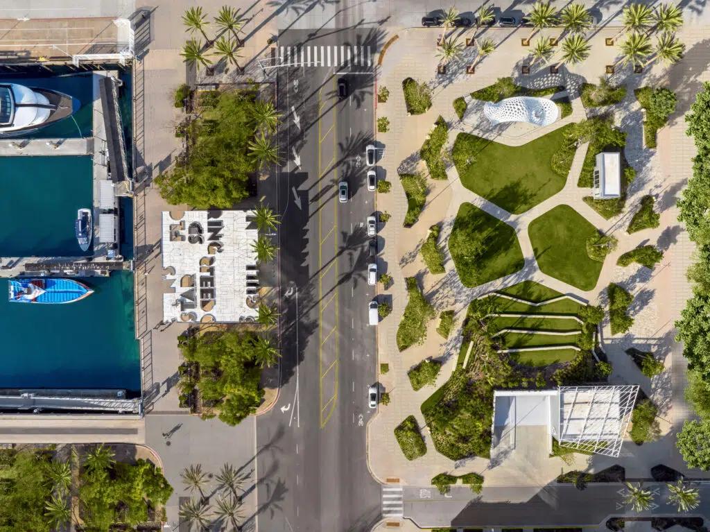 Aerial view of a waterfront streetscape and public plaza in San Diego designed by OJB Landscape Architecture, featuring palm-lined boulevards, sculpted lawns, curving pedestrian paths, and integrated seating areas that connect urban circulation with vibrant coastal open space.